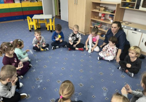 Dzieci rozmawiają z nauczycielką siedząc w kole na dywanie