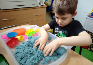 Chłopiec wykonuje ćwiczenia z piaskiem kinetycznym