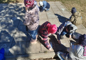 Dzieci maluja kredą w ogrodzie przedszkolnym