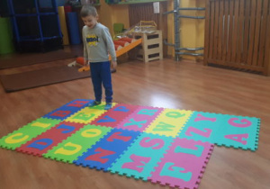 Chłopiec rozpoznaje litery skacząc na odpowiedni puzzel
