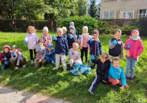 Dzieci zaopatrzone w rękawiczki pozują do zdjęcia przed budynkiem przedszkola