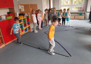 Dzieci ćwiczą równowagę chodząc po dużej literce M