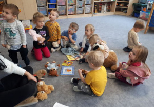 Dzieci siedzą na dywanie i prezentują swoje pluszaki