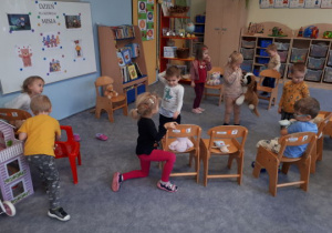 dzieci układają na krzesełku pluszaki według instrukcji nauczyciela
