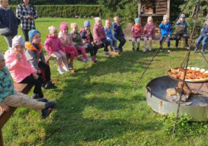 Dzieci siedzą na ławeczkach wokół ogniska