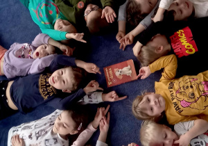Dzieci leżą na dywanie z kolejną pozycją książkową