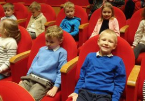 Dzieci siedzą w fotelach na widowni w oczekiwaniu na spektakl