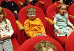 Dzieci siedzą w fotelach na widowni w oczekiwaniu na spektakl