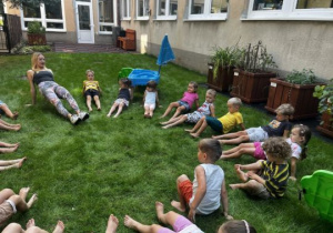 Dzieci wykonują ćwiczenia w pozycji leżącej na trawie