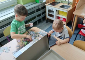 Jeden chłopiec układa puzzle, a drugi chłopiec rysuje na tabliczce magnetycznej