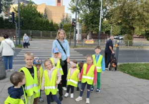 Dzieci stoją na chodniku w kamizelkach odblaskowych