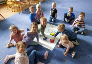 Dzieci siedzą na dywanie i grają w dużą grę planszową