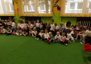 Dzieci siedzą na ławeczkach i dywanie