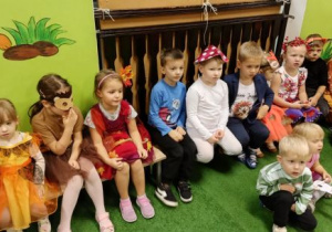 Dzieci w jesiennych strojach siedzą na ławeczkach