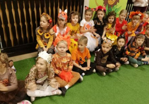 Dzieci w jesiennych strojach siedzą na ławeczkach
