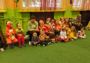 Dzieci w jesiennych strojach siedzą na ławeczkach