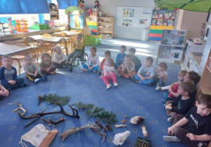 Dzieci siedzą na dywanie i obserwują zebrane eksponaty