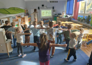 Dzieci stoją na dywanie z rękami do boku