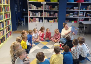 Dzieci siedzą na dywanie i słuchają opowiadania